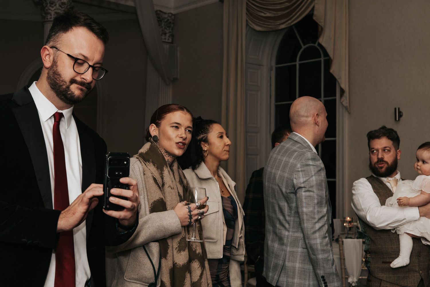 Wedding guests in formal attire mingle and chat during an elegant indoor reception event.