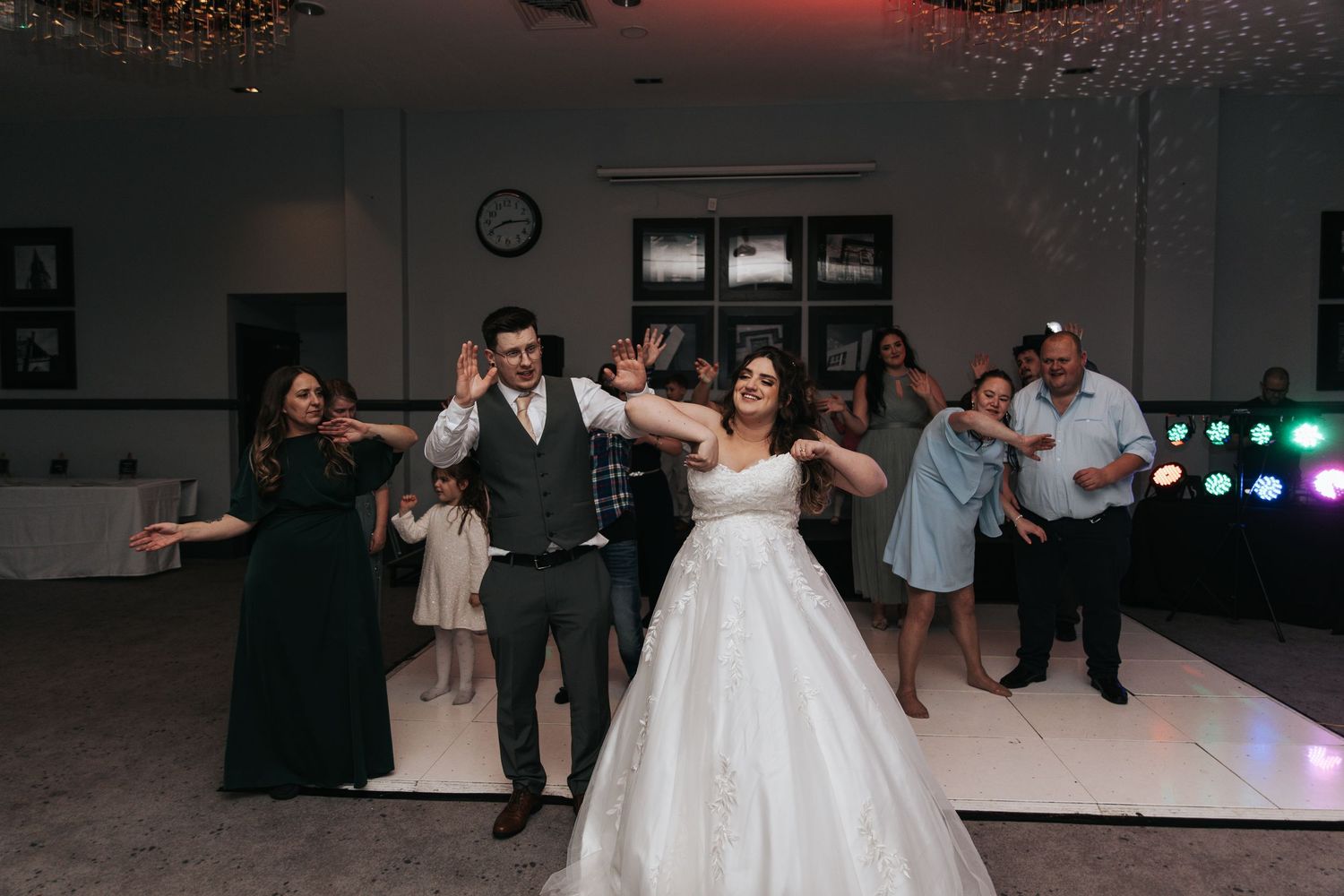 Wedding party members dancing together on a white dance floor with colorful lights in the background.