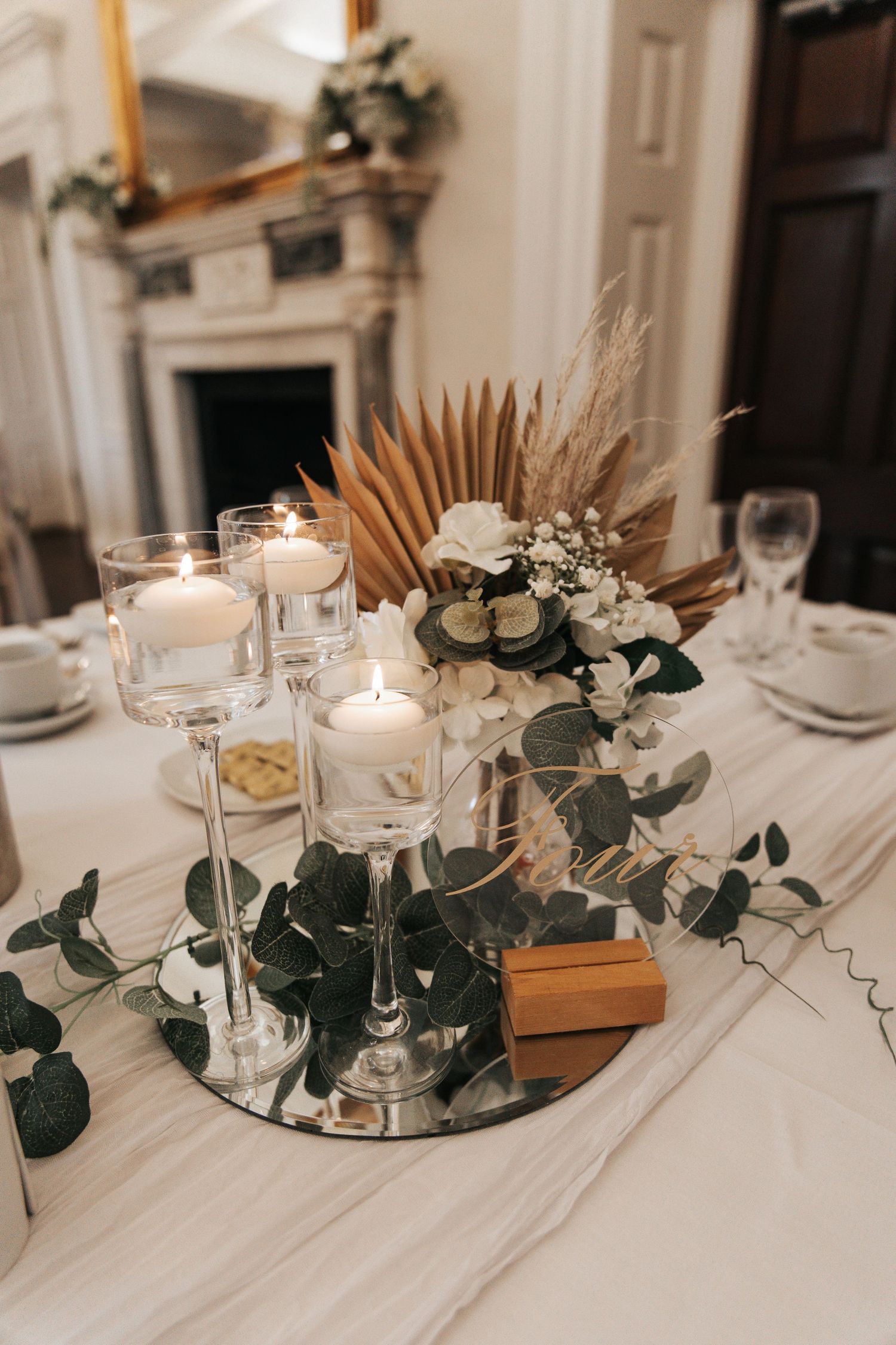 Elegant wedding table setting with white flowers, eucalyptus, and glowing candles on mirror bases.