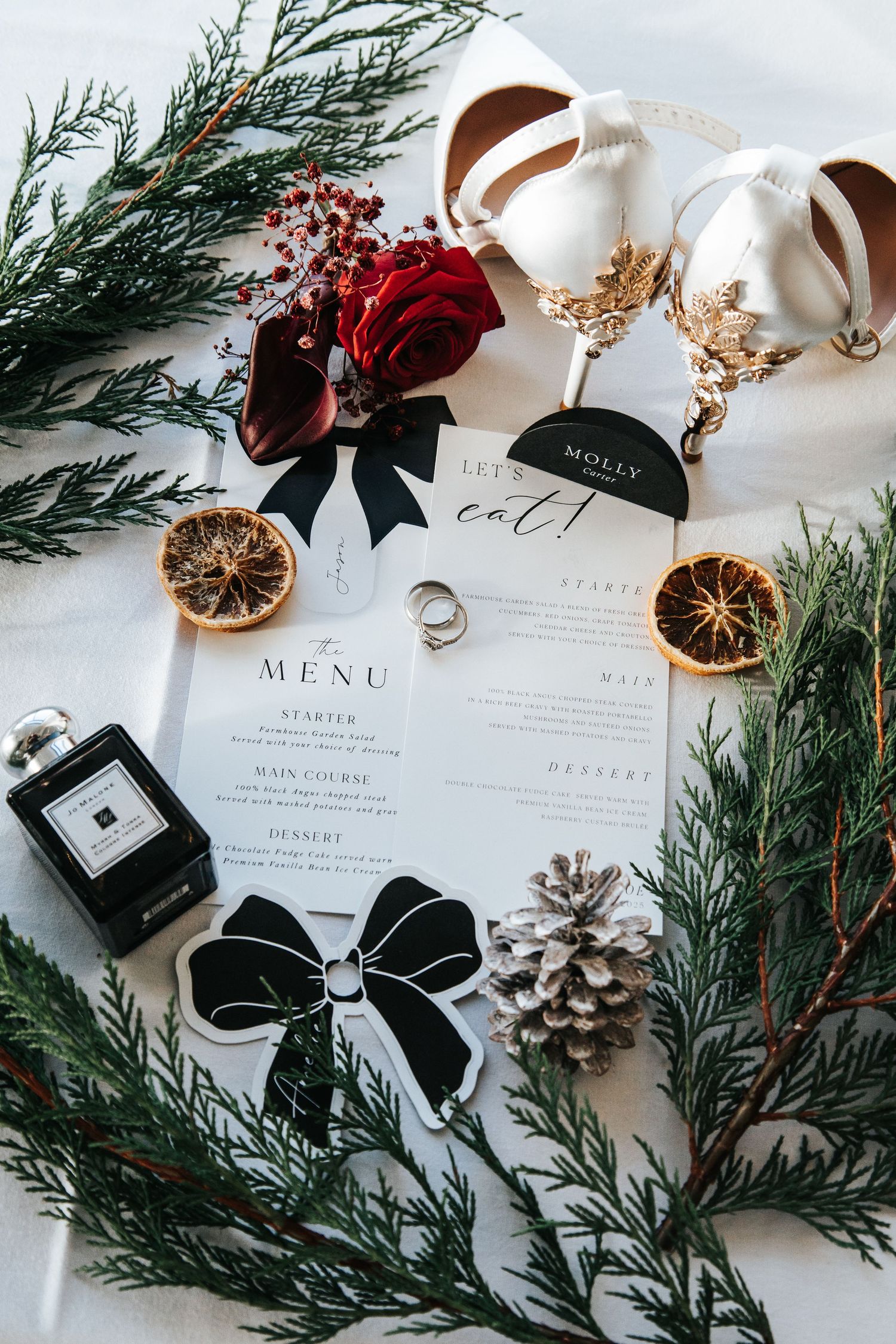 Winter wedding details with menu cards, evergreen sprigs, dried oranges and black ribbon accents.
