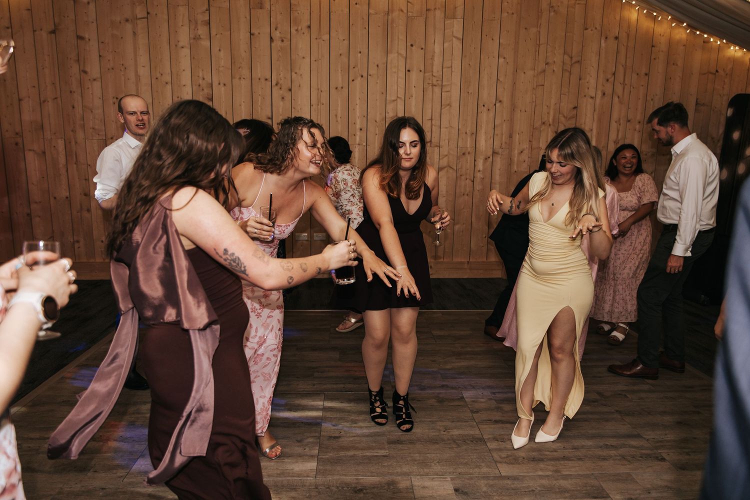 Guests dancing joyfully at a wedding reception in a rustic wood-paneled venue.