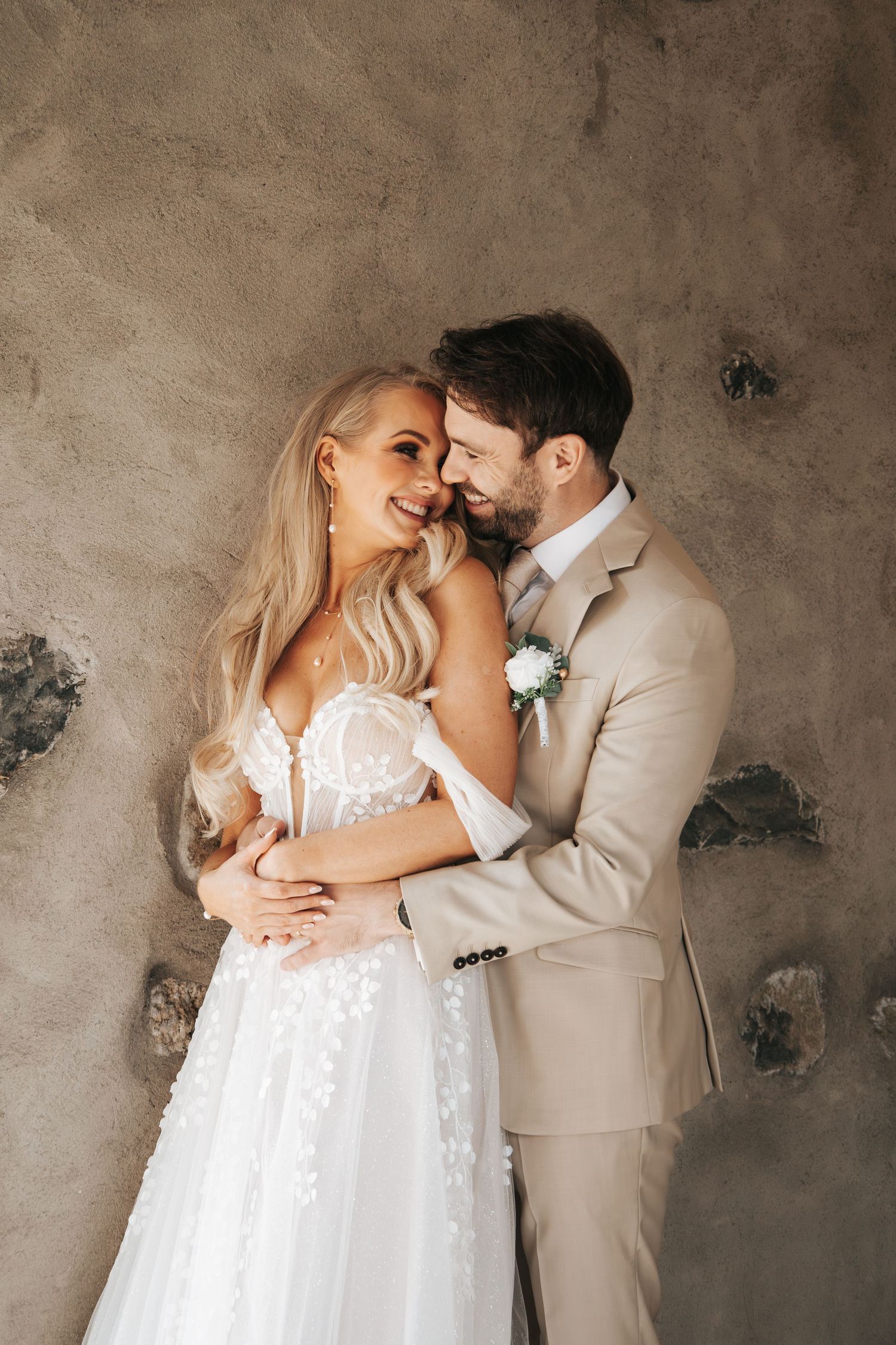 Romantic wedding portrait against textured wall showing tender embrace.