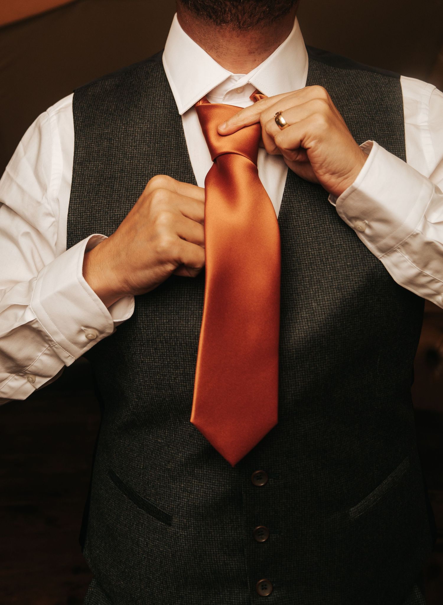 Step-by-step sequence of adjusting an orange tie with a dark suit.
