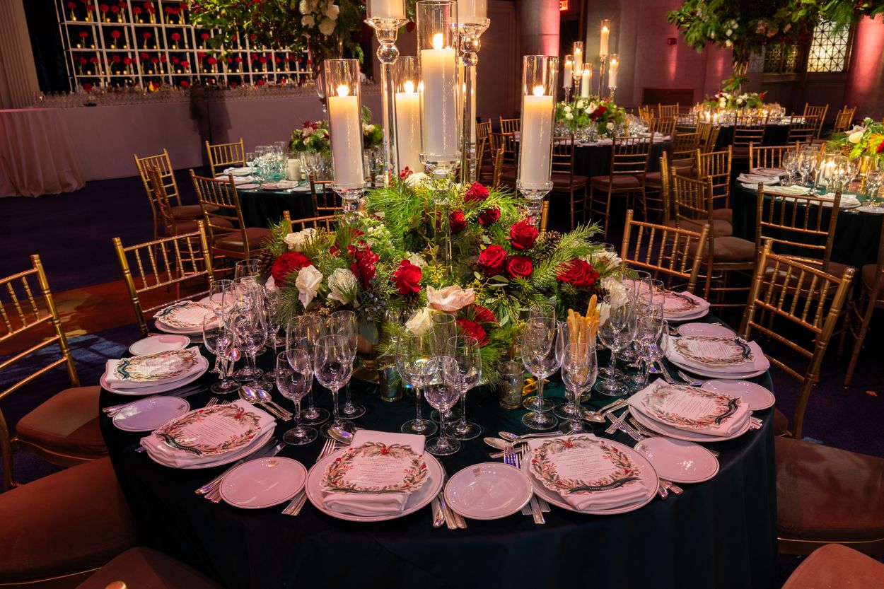 Round dining tables set for an elegant reception with dark linens and floral centerpieces.