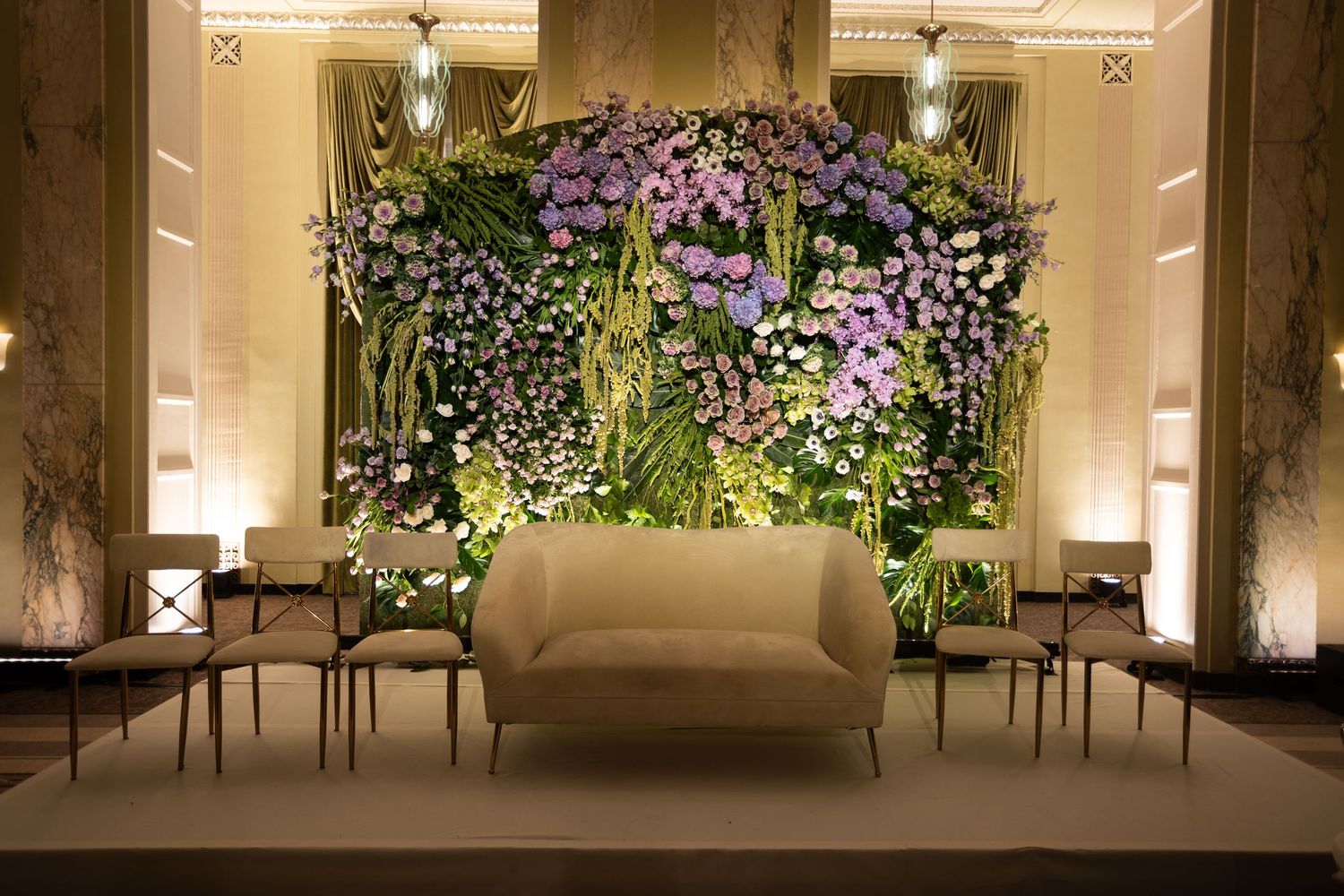 Elegant lounge area featuring a beige sofa against a lush purple and white floral wall installation.