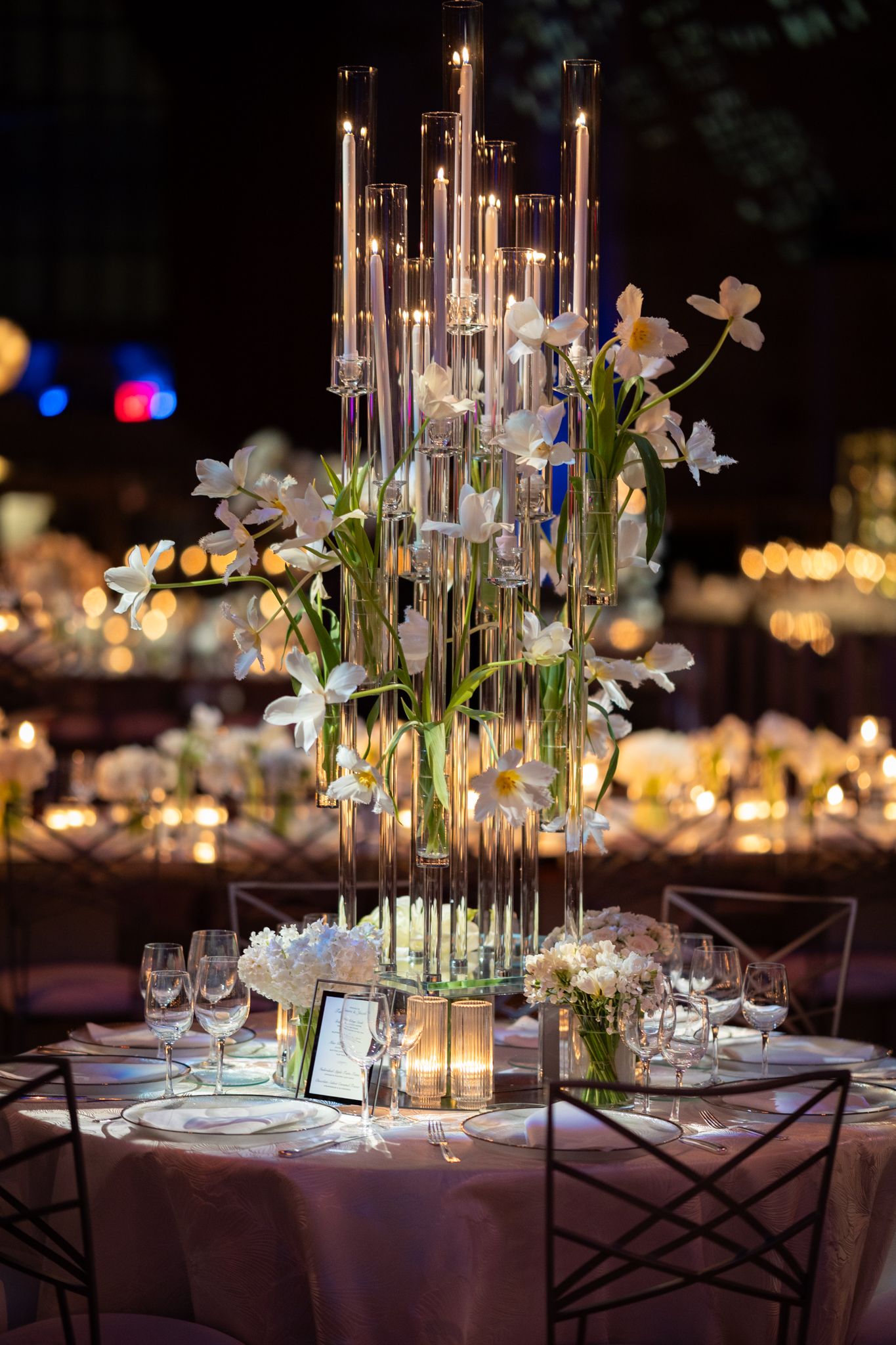 Stunning tall glass centerpiece with cascading white orchids and glowing candles on an elegant wedding reception table.