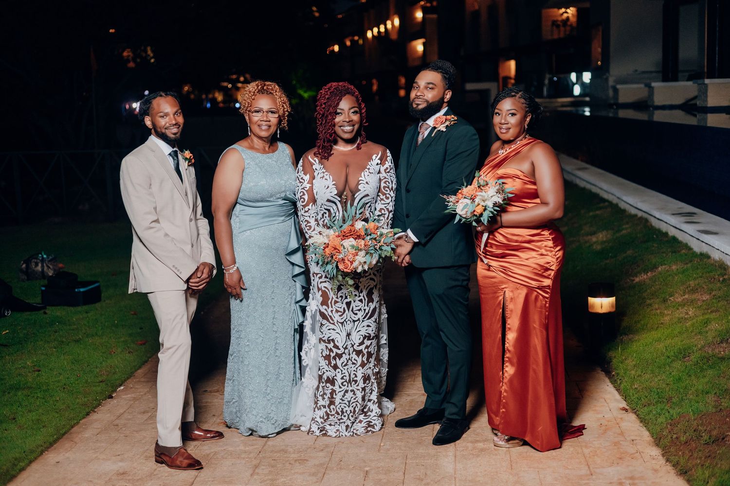 A formal group poses for an evening photograph on a lawn, wearing elegant gowns and suits.