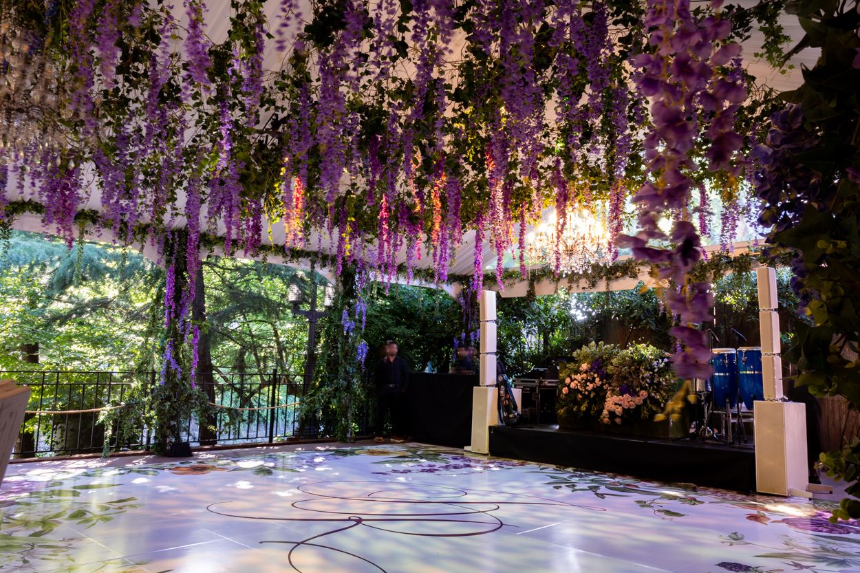 Enchanting garden path illuminated with purple wisteria flowers and string lights creating a magical tunnel effect.