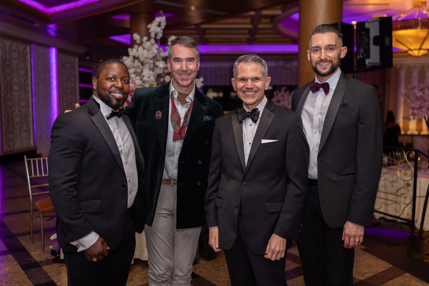 A group of people in formal attire smiling and posing together at an elegant event with purple lighting.
