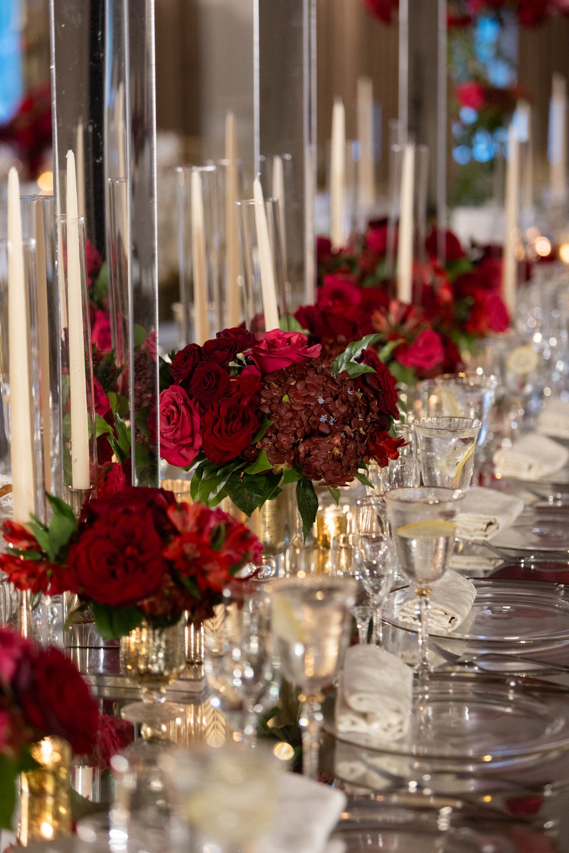 Luxurious table setting with deep red roses, tall candles, and crystal glassware for an upscale event.