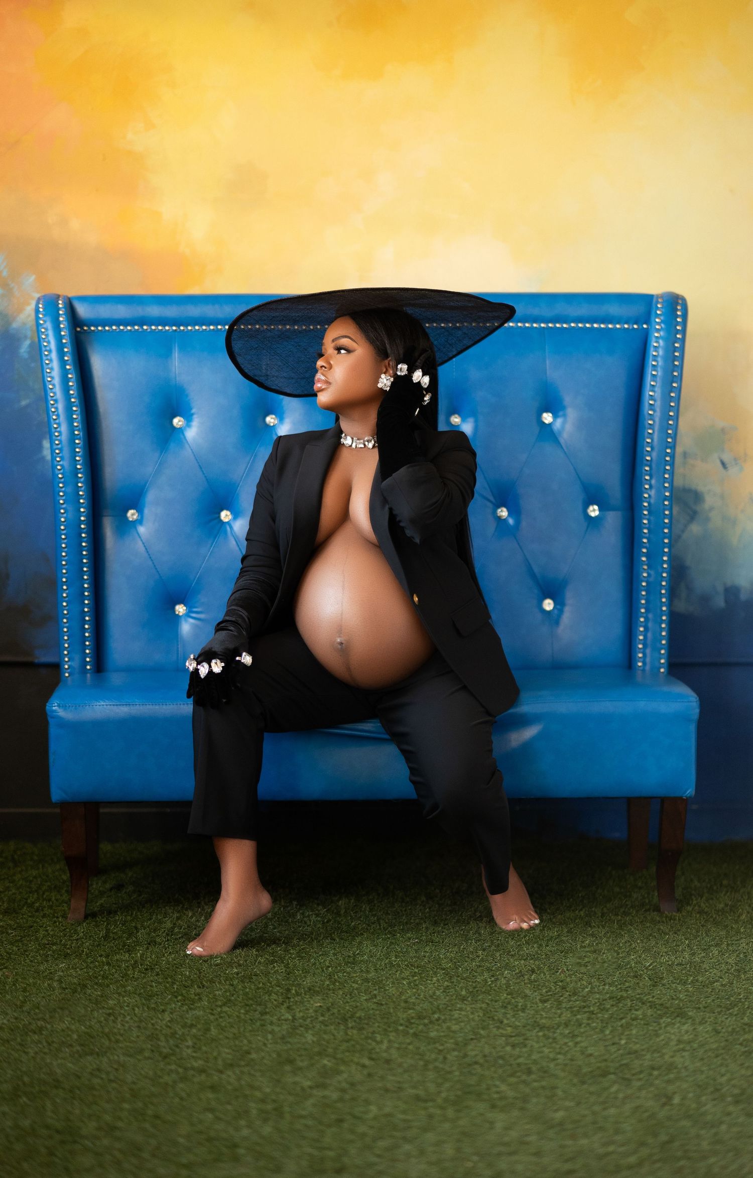 Artistic maternity photo series showing a woman in black dress reclining on a tufted blue velvet bench against golden backdrop.