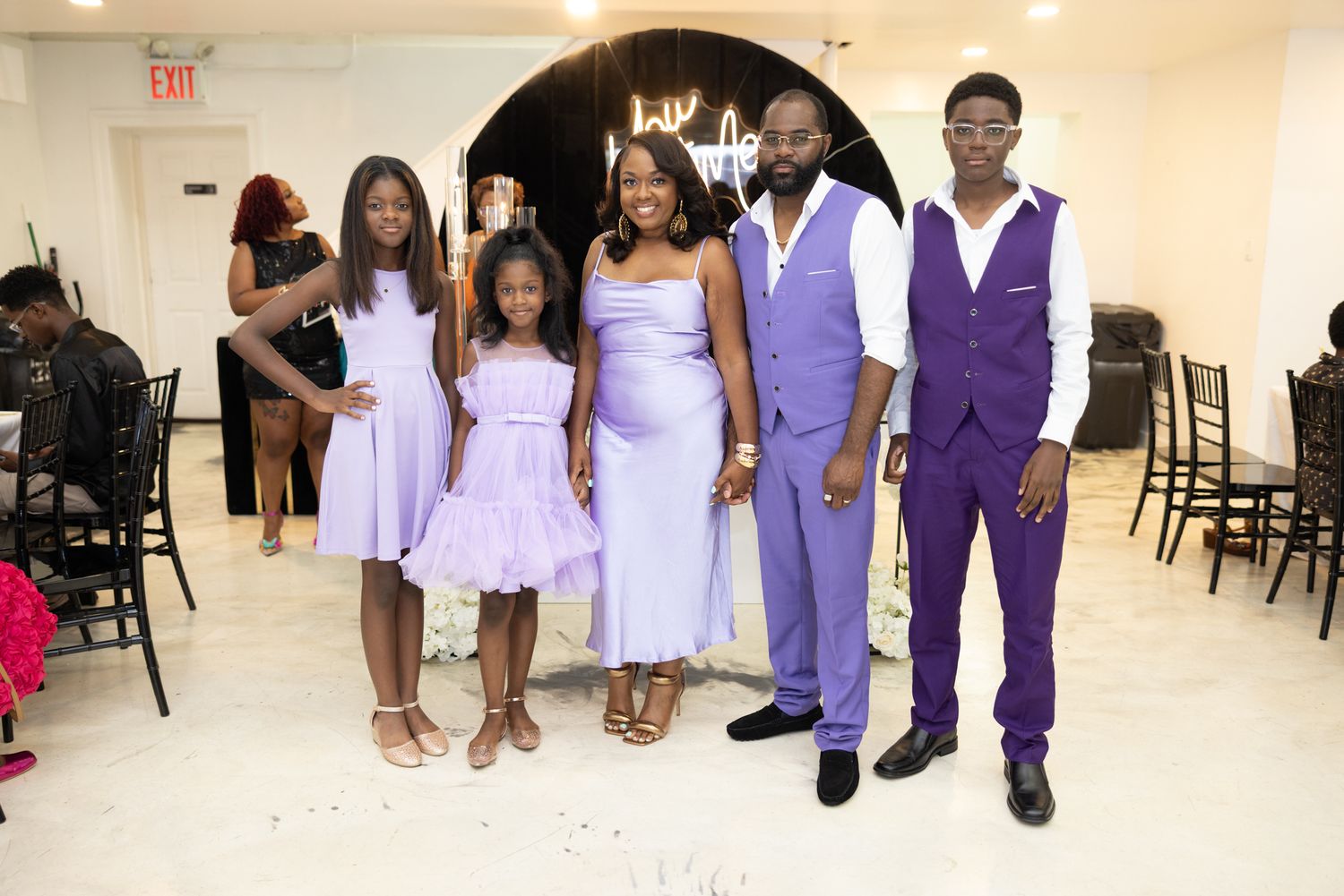 A wedding party poses together in matching purple and white formal attire at an indoor venue.