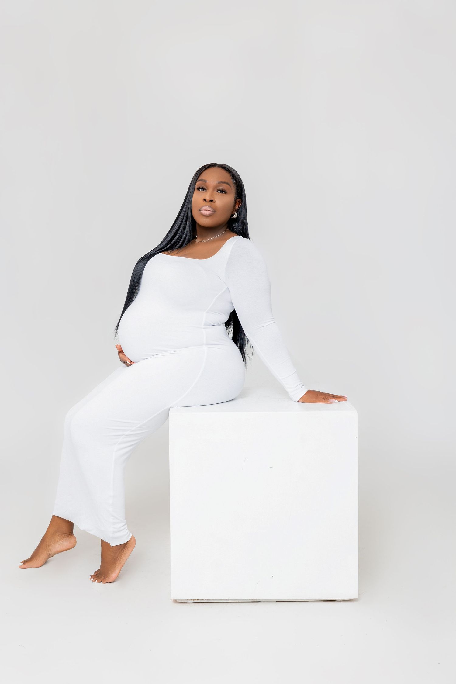 Model in white bodycon dress poses on white cube furniture against light background showing different angles.