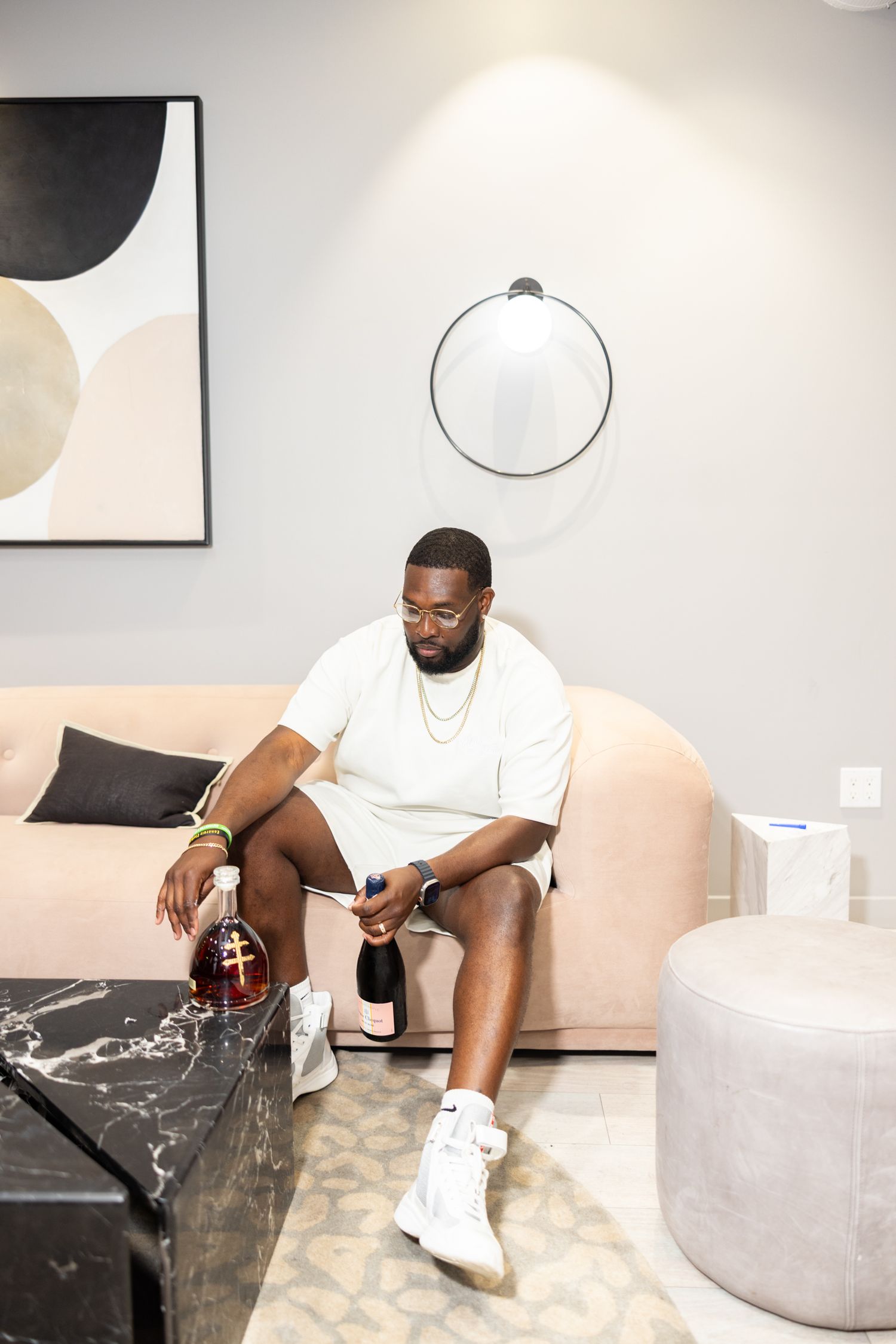 A series of photos showing someone sitting on a modern gray sofa in a minimalist room with abstract wall art.