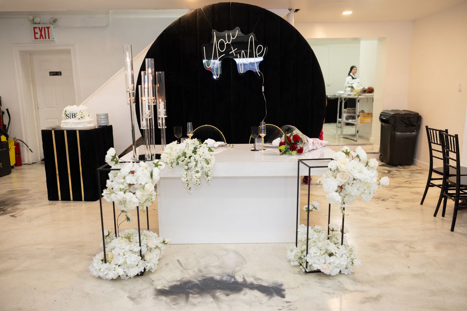 Elegant wedding reception setup featuring a white table with floral arrangements under a black arch.