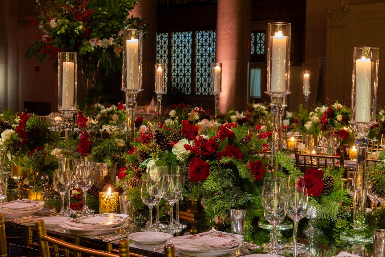 Luxurious wedding reception decor featuring candlelit tables adorned with red roses and greenery garlands.