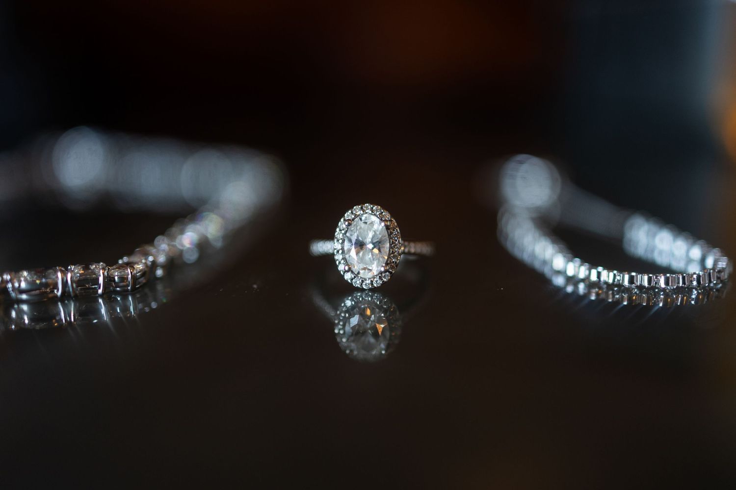 Close-up macro shot of sparkling diamond engagement rings and wedding bands on dark reflective surface.