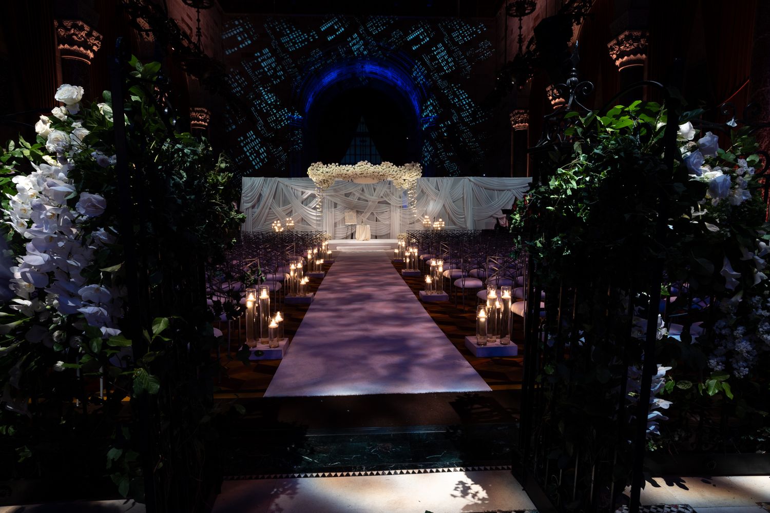 Elegant wedding ceremony aisle with illuminated path and floral archway decorated with white flowers and candlelight.