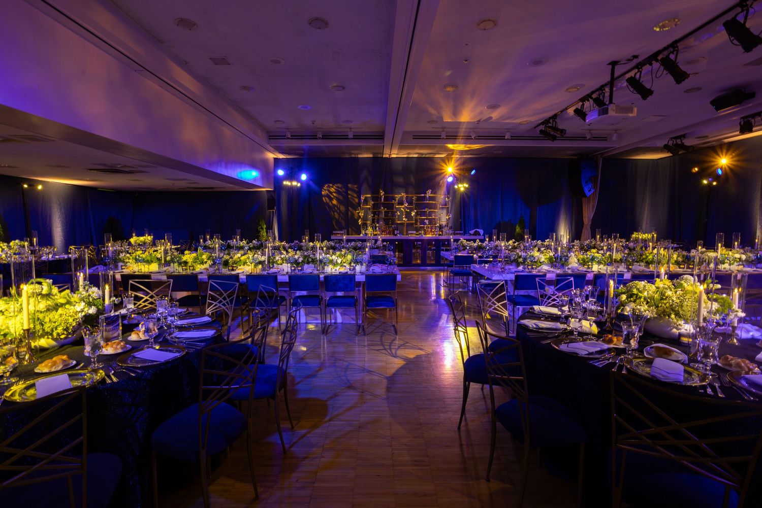 Modern reception hall with tables set under blue and yellow ambient lighting creating a dramatic atmosphere.