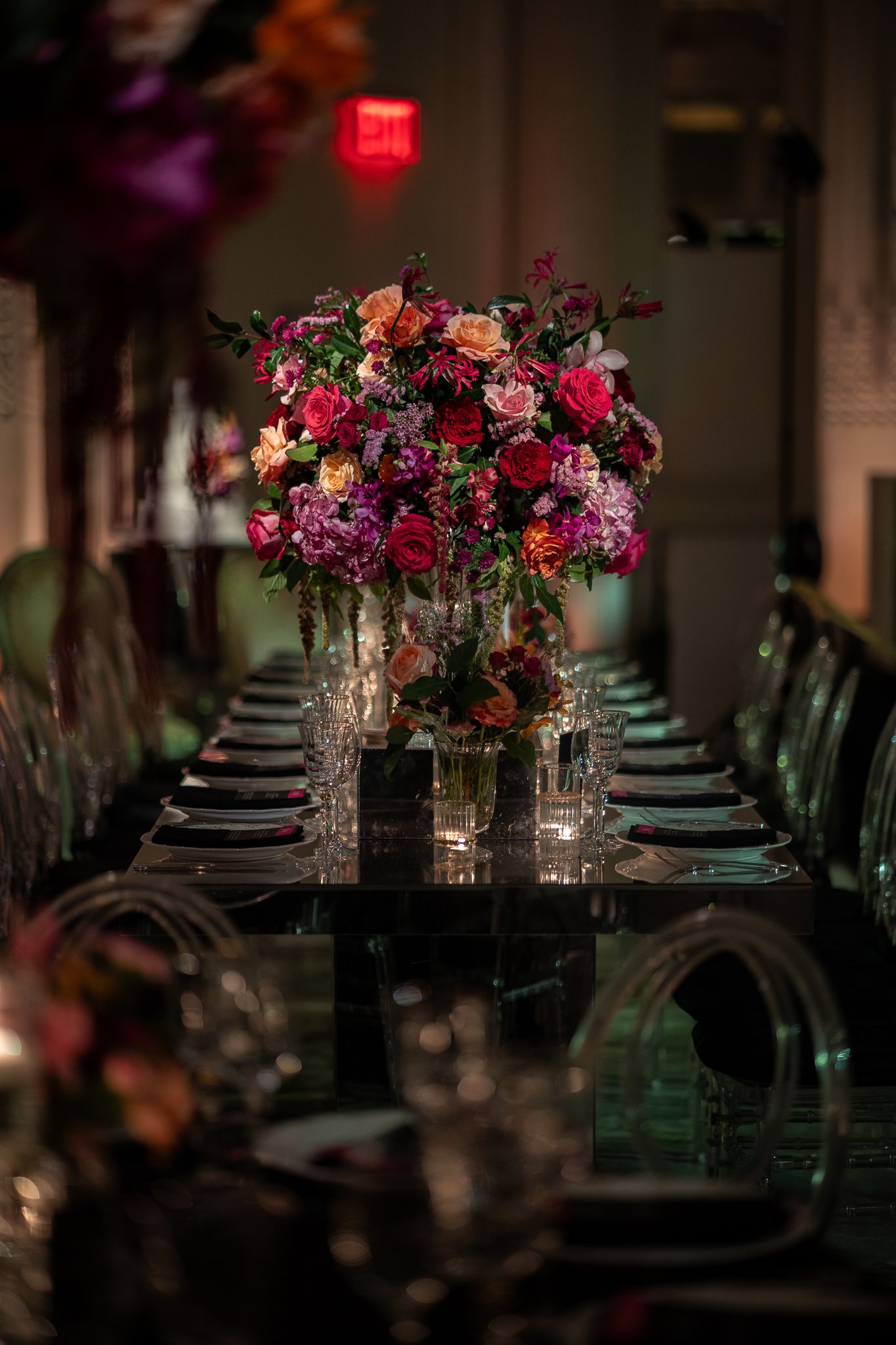 Romantic wedding reception table setting with vibrant purple and pink floral centerpieces and moody lighting.