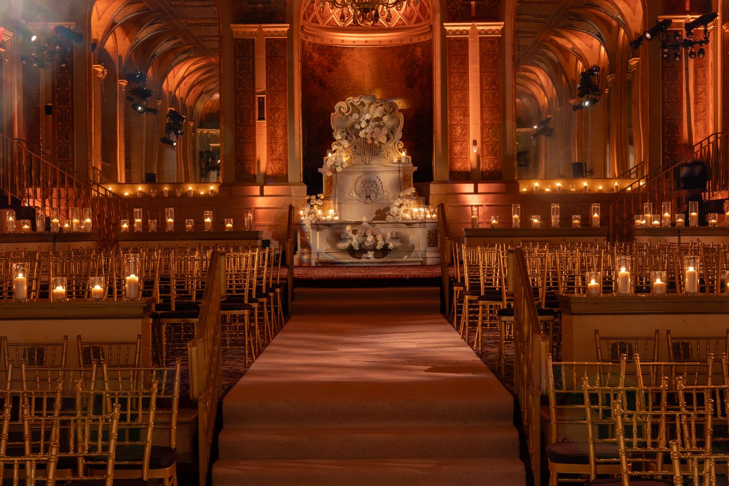 Ornate ballroom with amber lighting and rows of chiavari chairs set for a ceremony.