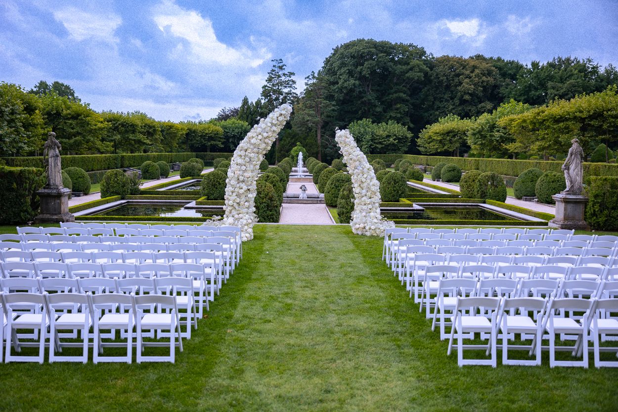Outdoor wedding ceremony setup with white chairs arranged on a green lawn under blue skies.