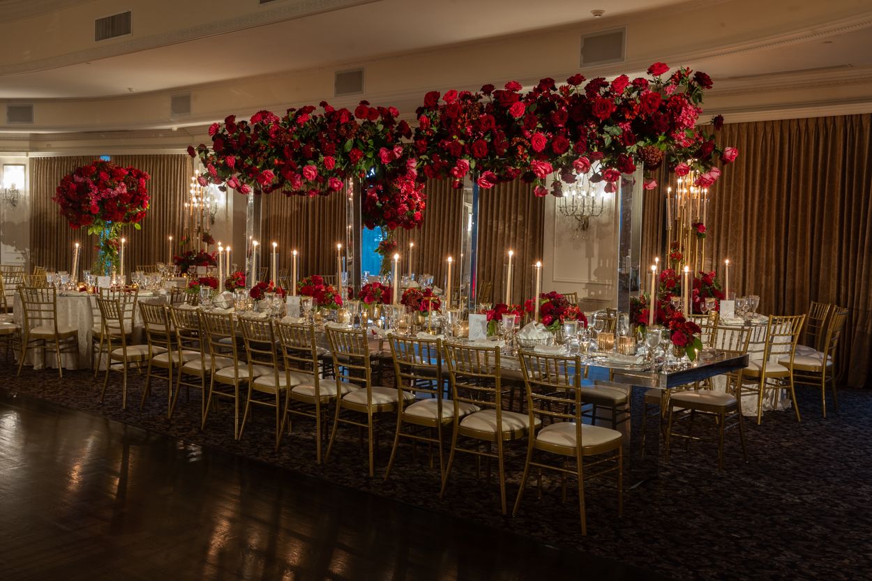 Grand reception hall with dramatic lighting and red floral centerpieces along dining tables.