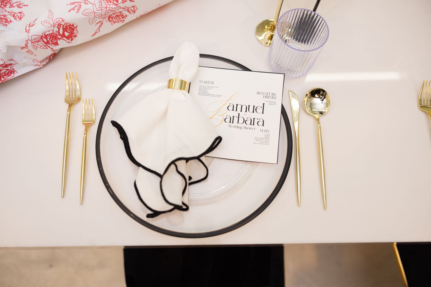 Place setting with gold utensils and black plate on white tablecloth at formal event.