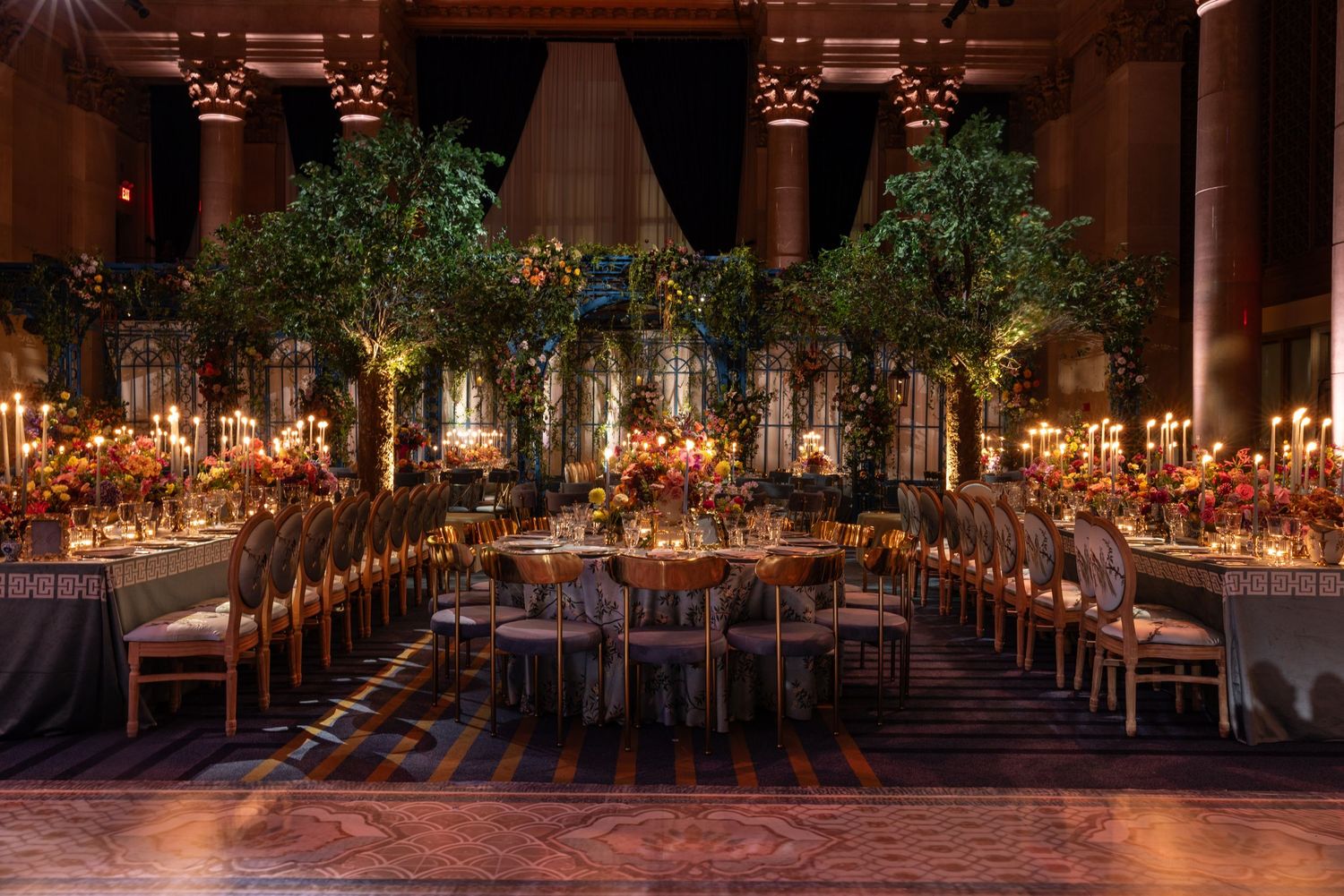 Elegant candlelit wedding reception tables arranged in long rows beneath twinkling lights in a rustic indoor venue.