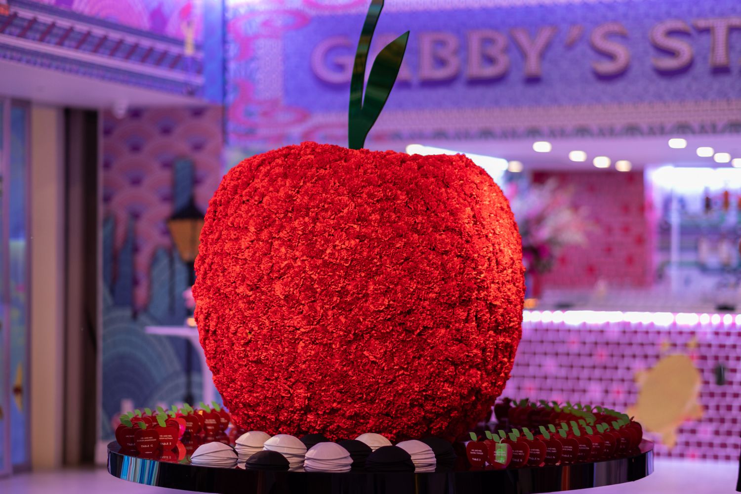 Vibrant red rose arrangements and dessert displays illuminated by purple ambient lighting.