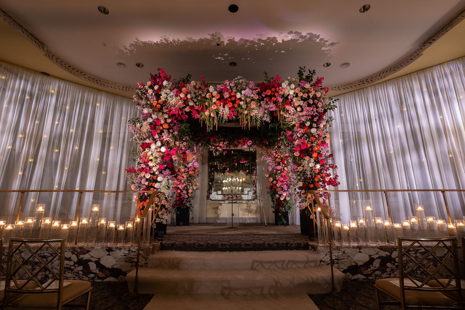 Romantic wedding venue with pink floral ceiling installations and sheer white drapery.
