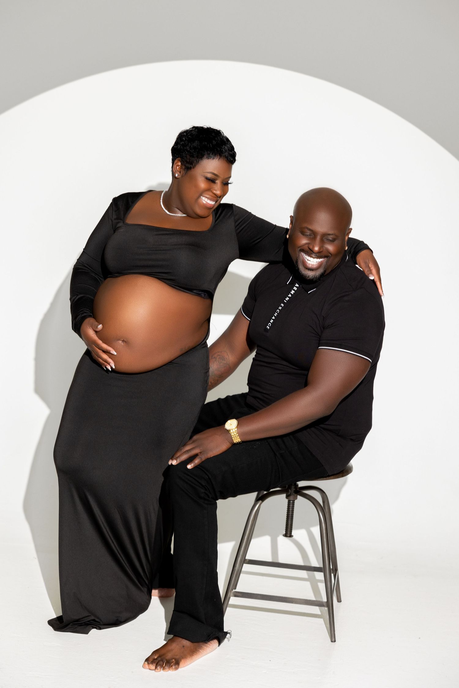 A series of artistic maternity photos showing a pregnant person in black clothing posing on a white chair against a light background.