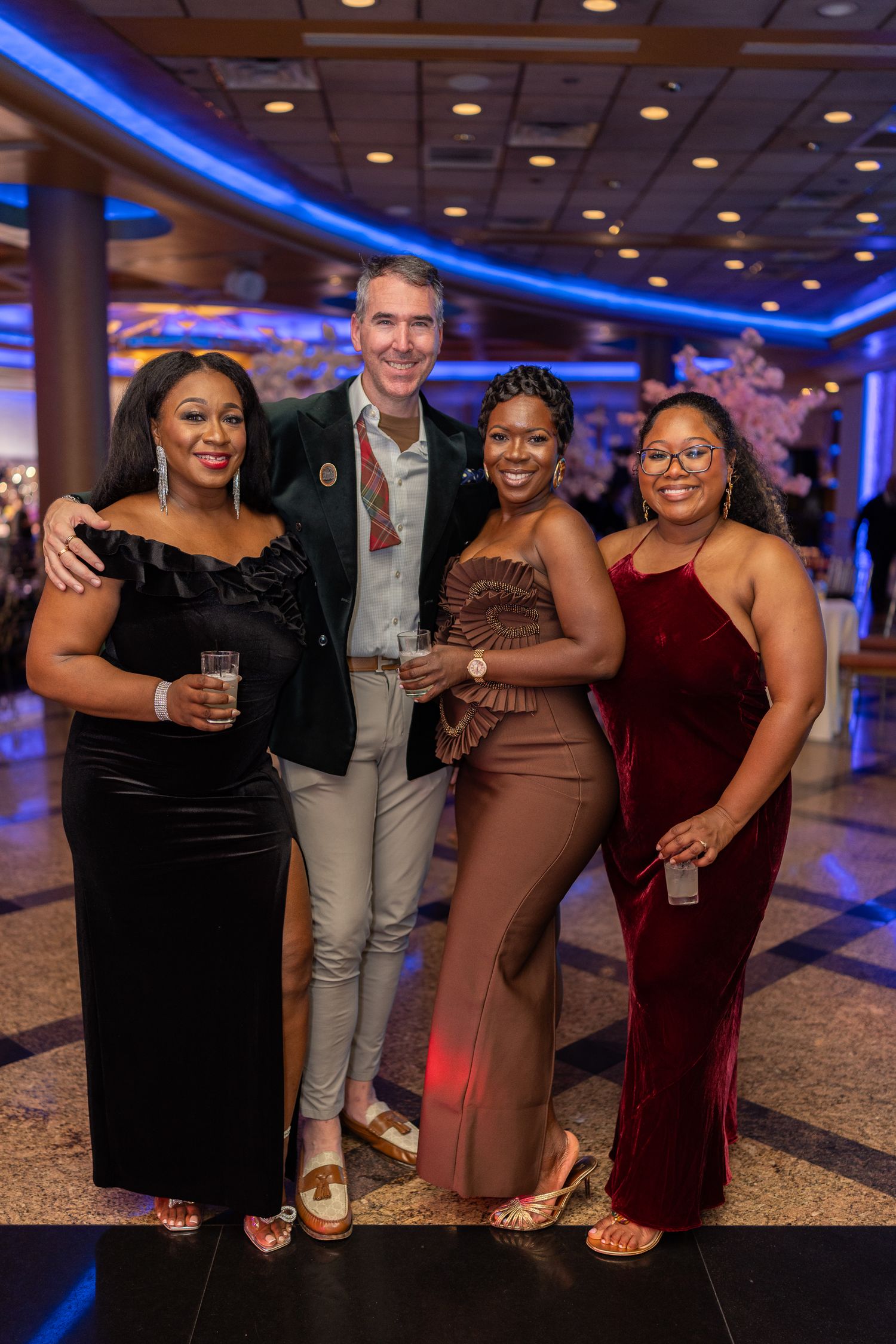 A group of friends pose together at an elegant event with blue lighting and decorative interior in the background.