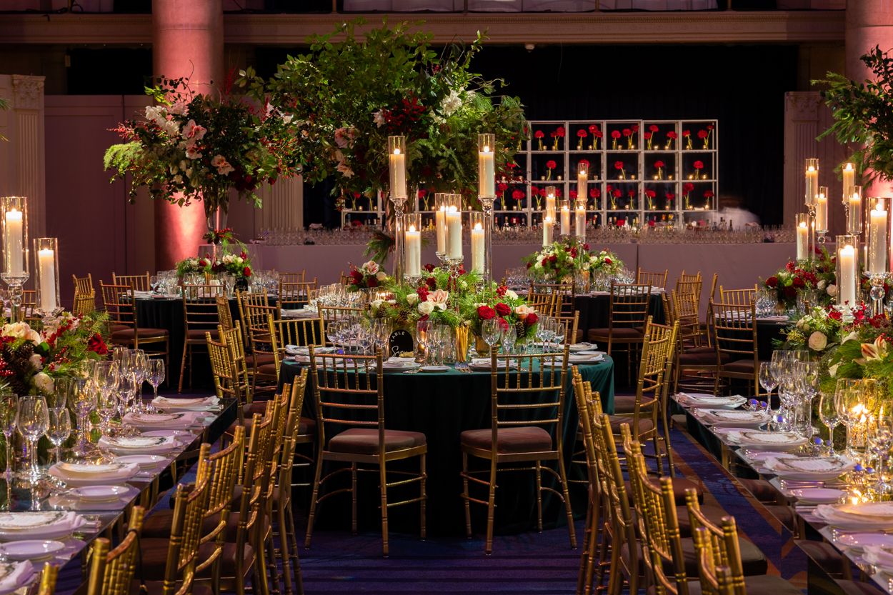 Long banquet tables set for an elegant wedding reception with gold chairs and lush floral arrangements.