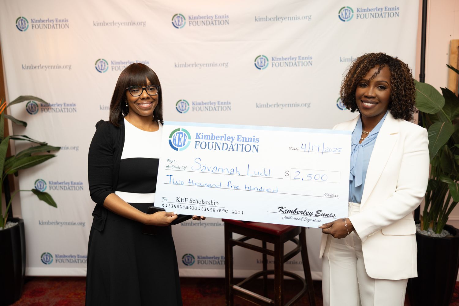People holding award checks and certificates pose in front of a branded backdrop at a foundation event.