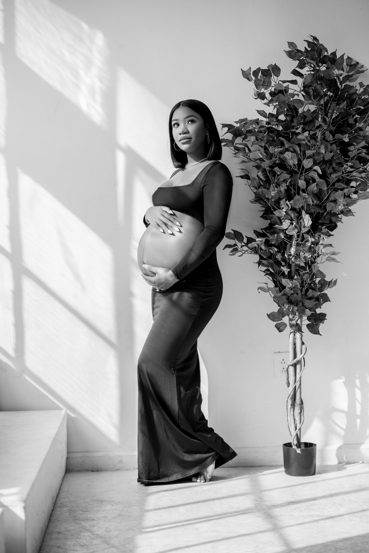 A series of black and white maternity photos showing an expectant mother in a dark dress against a white wall with shadows.