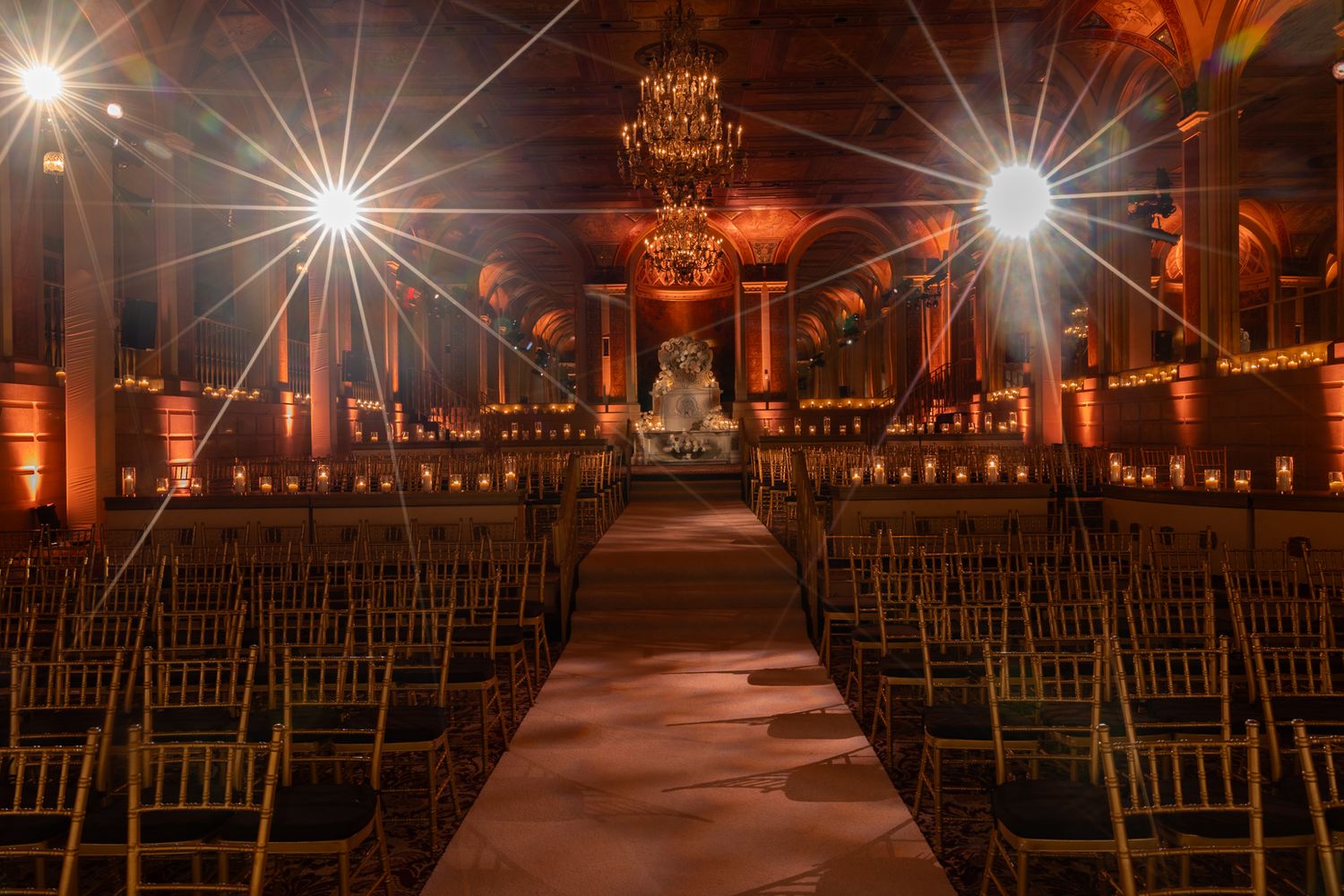 Elegant wedding venue setup with rows of wooden chairs under dramatic evening lighting and ornate chandeliers.