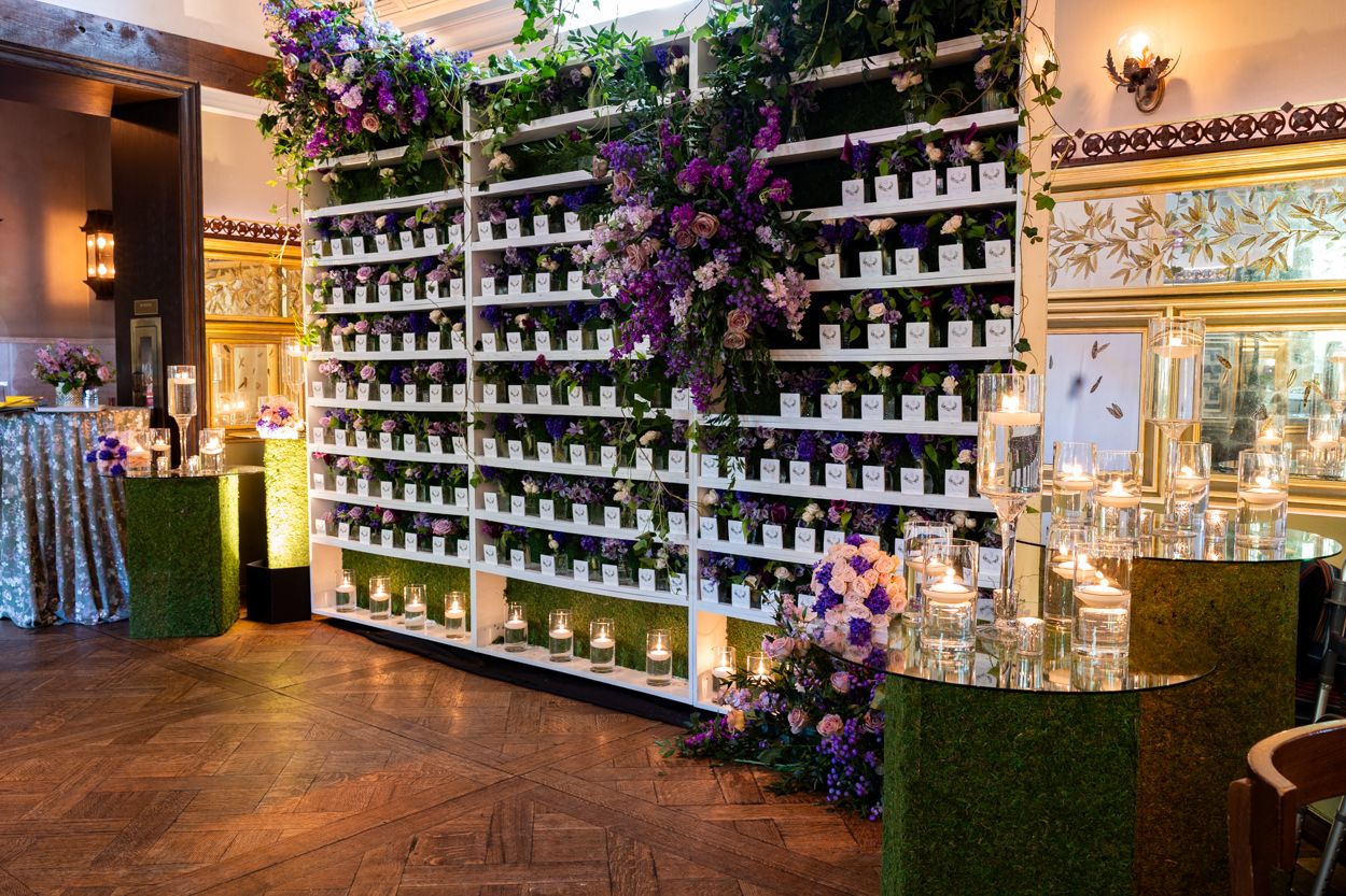 Long display wall of perfume bottles illuminated on white shelves with purple floral accents.