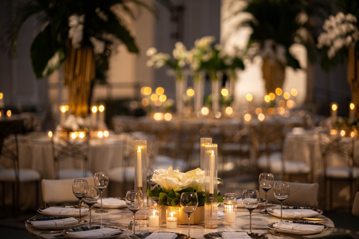 Intimate wedding reception setup with glowing candles and elegant table settings in warm lighting.