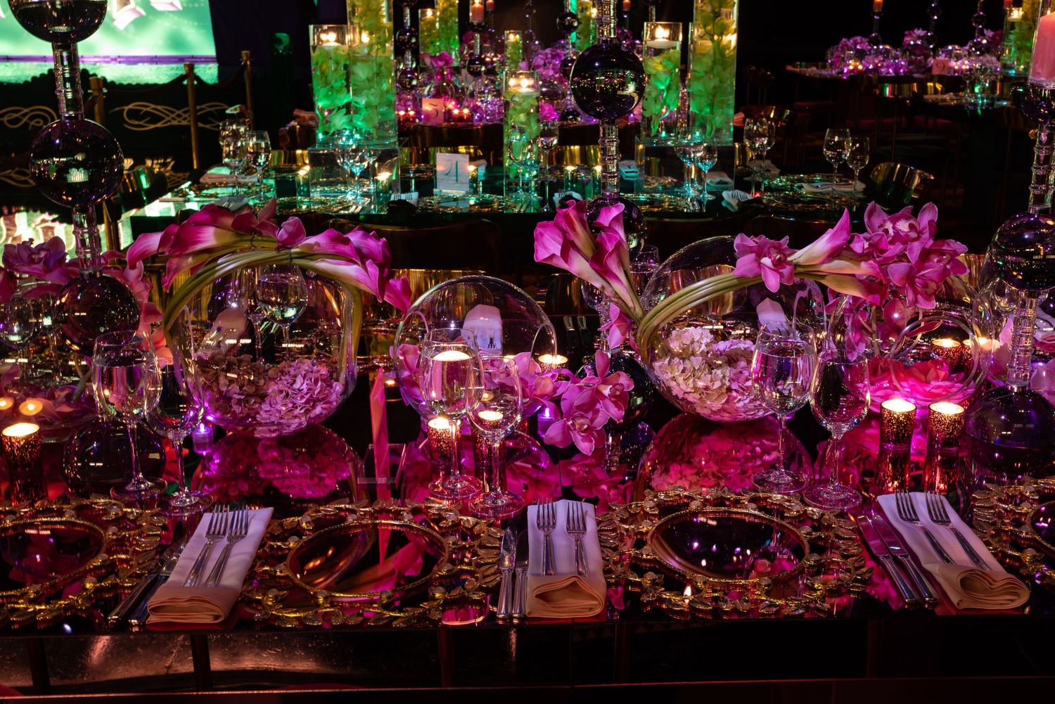 Elegant wedding reception venue with vibrant pink and purple lighting illuminating floral centerpieces and table settings.