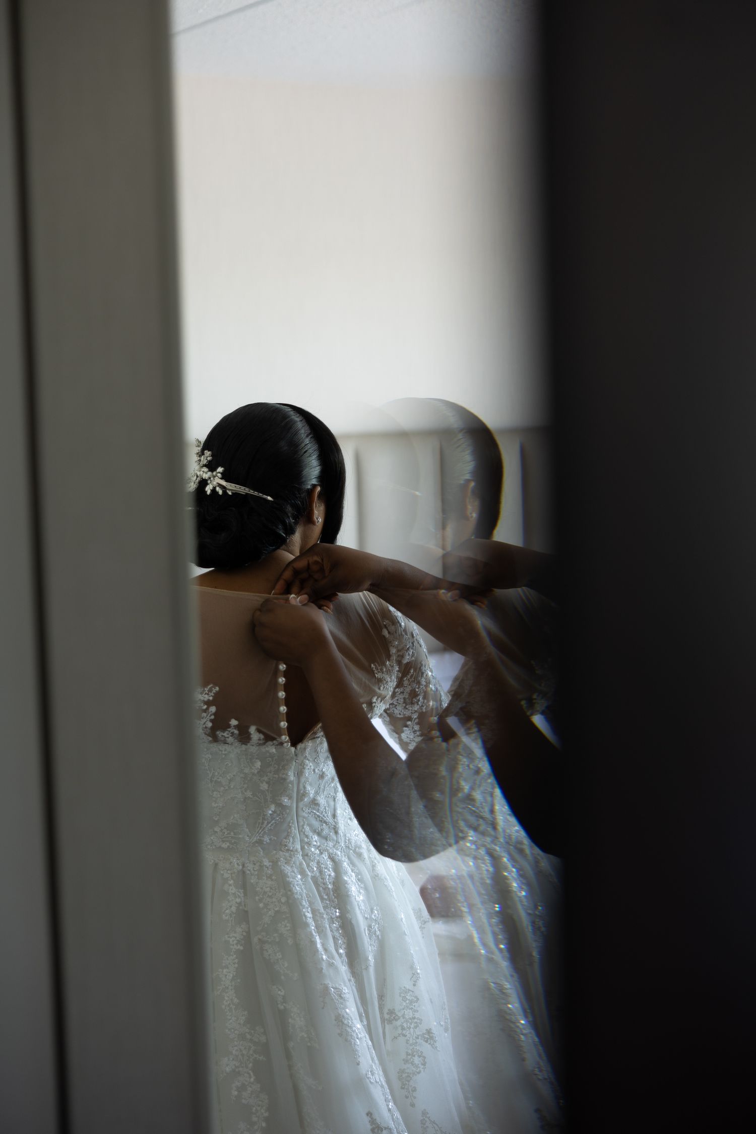 An artistic silhouette shot shows a wedding dress being fitted in front of a mirror.