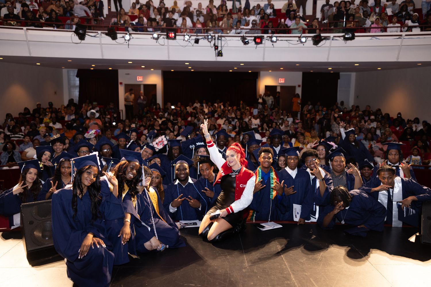 Large crowd of students in blue graduation gowns sitting together in an auditorium during a ceremony.