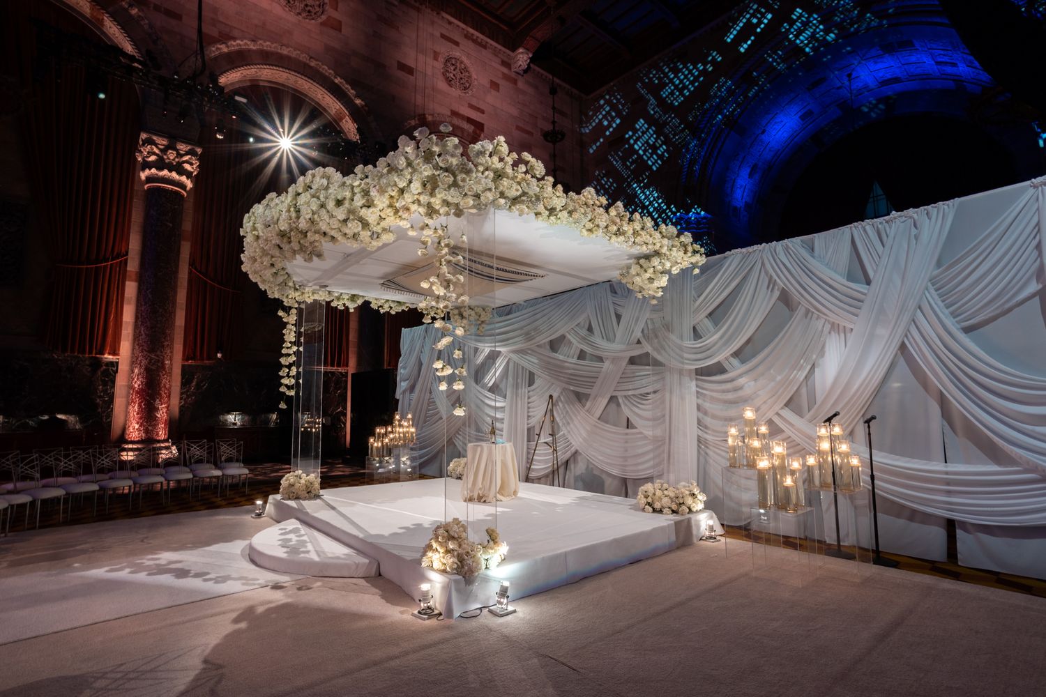 Elegant wedding reception venue with dramatic blue lighting and white floral centerpieces on round tables.