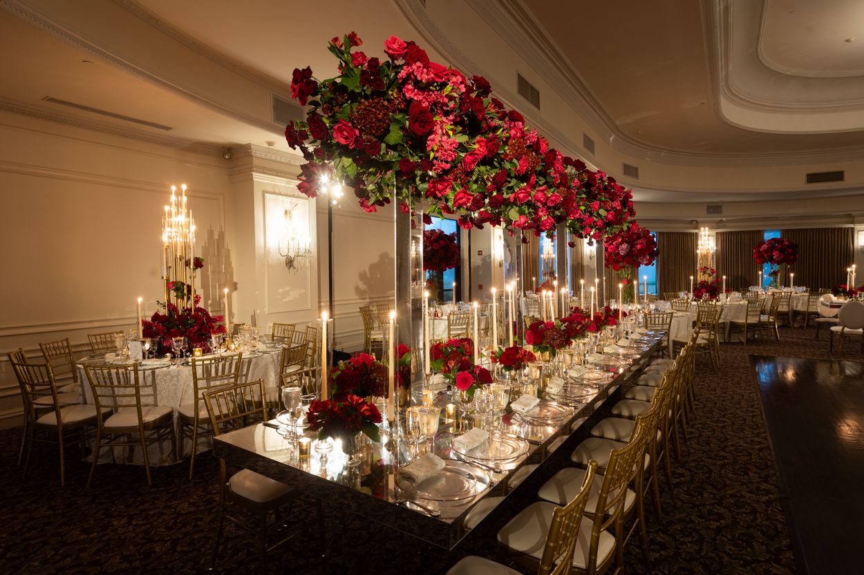 Elegant wedding reception tables decorated with red roses and glowing candelabras in a dimly lit ballroom.