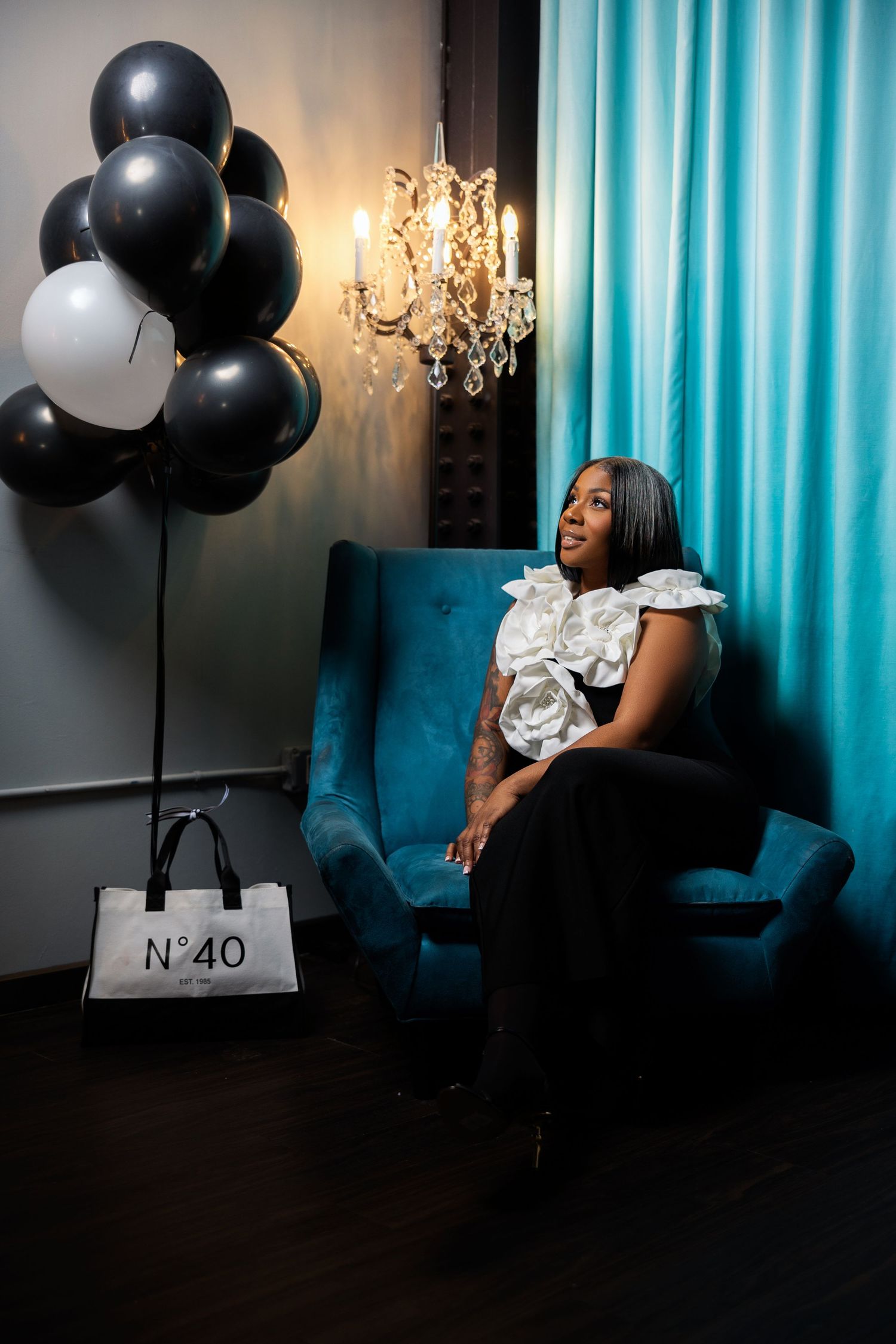 A woman in a dark room with black balloons and turquoise curtains poses for a dramatic photo series.