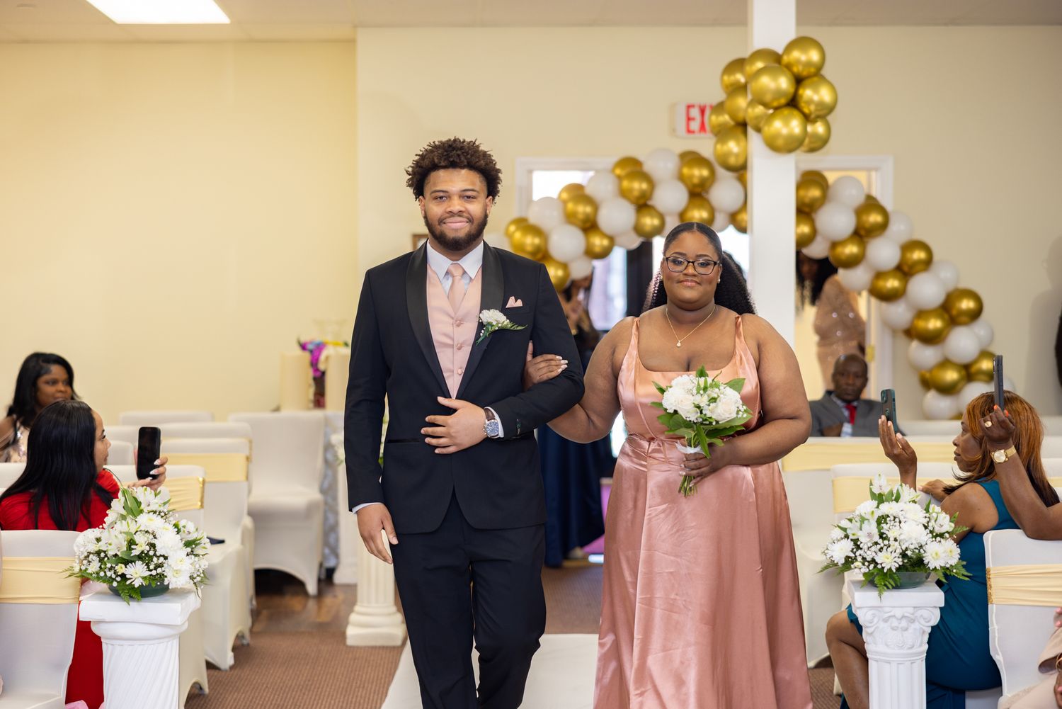A wedding celebration in a venue decorated with gold balloons and floral arrangements.