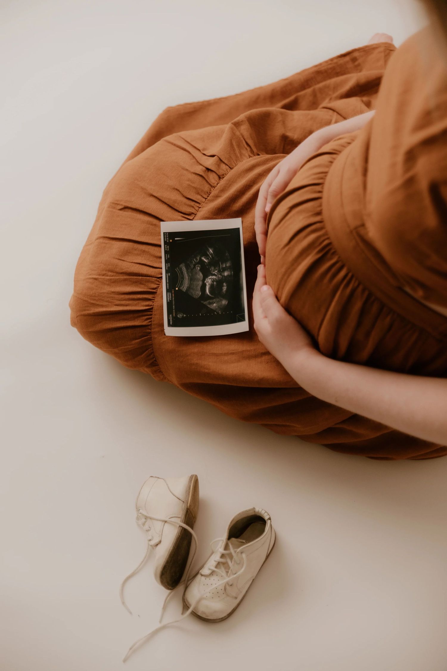 A series of warm brown maternity photos showing a pregnant belly with small baby shoes in minimalist style.