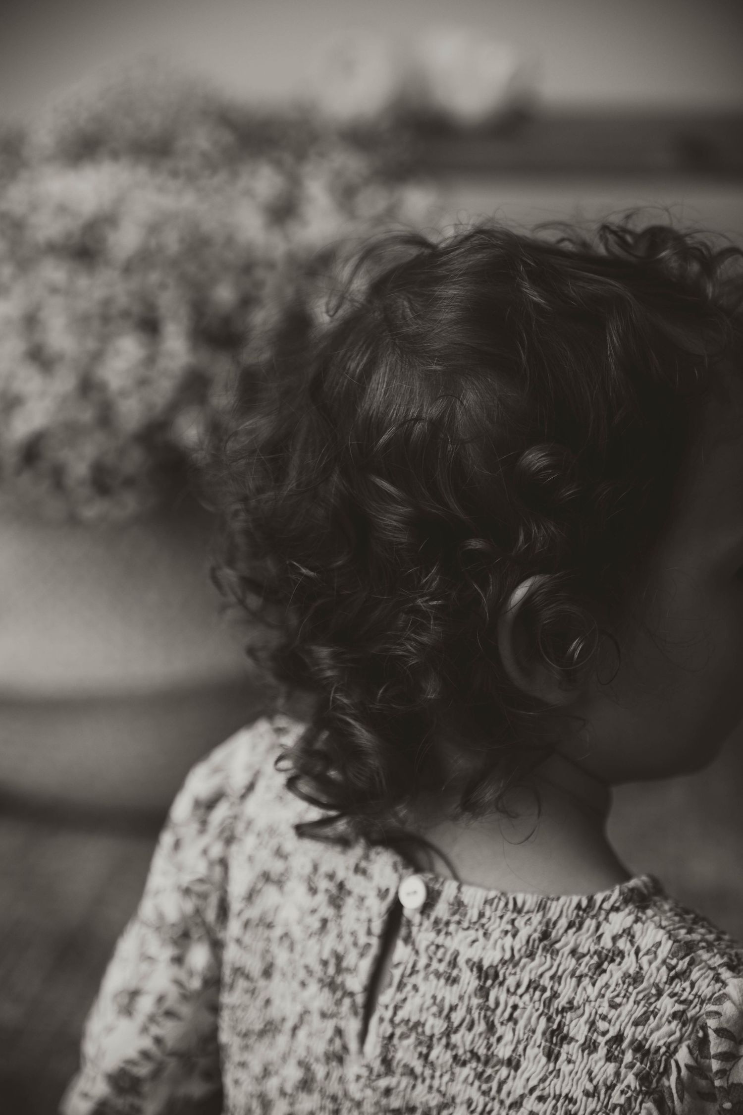 Close-up black and white portrait showing curly hair and patterned clothing against a dark background.