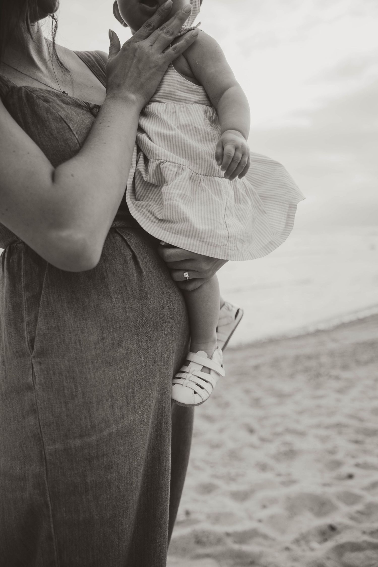 Close-up shots of a small child being held in casual clothing on a sandy beach.