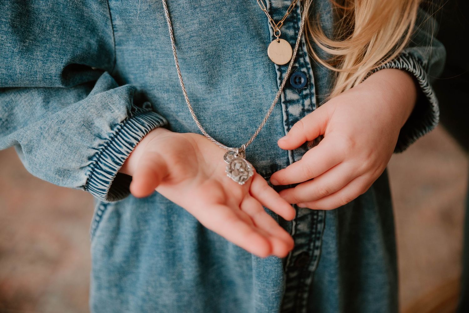 Close-up of hands in blue denim fabric holding a sentimental necklace in natural light.